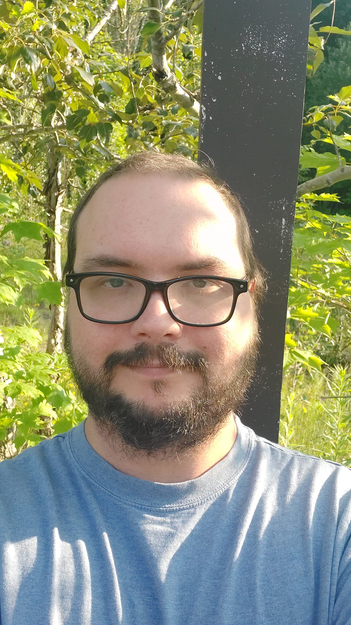 A man is dressed in a t-shirt standing in front of a lamp post looking stoned